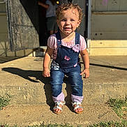 Amiliyah is registered to the contest to win money with this photo: toddler, child, curly_hair, denim_overalls, pink_shirt, sandals, outdoor, sunlight, shadow, concrete_step, grass, smiling, face, person, front_yard, daylight, cute, happy, young_child, portrait