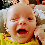 Elijah is registered to the contest to win money with this photo: baby, smiling, winking, yellow_clothing, face, infant, hand, blanket, indoor, happy, closeup, skin, furniture, couch, expression, child, portrait, cute, person, young