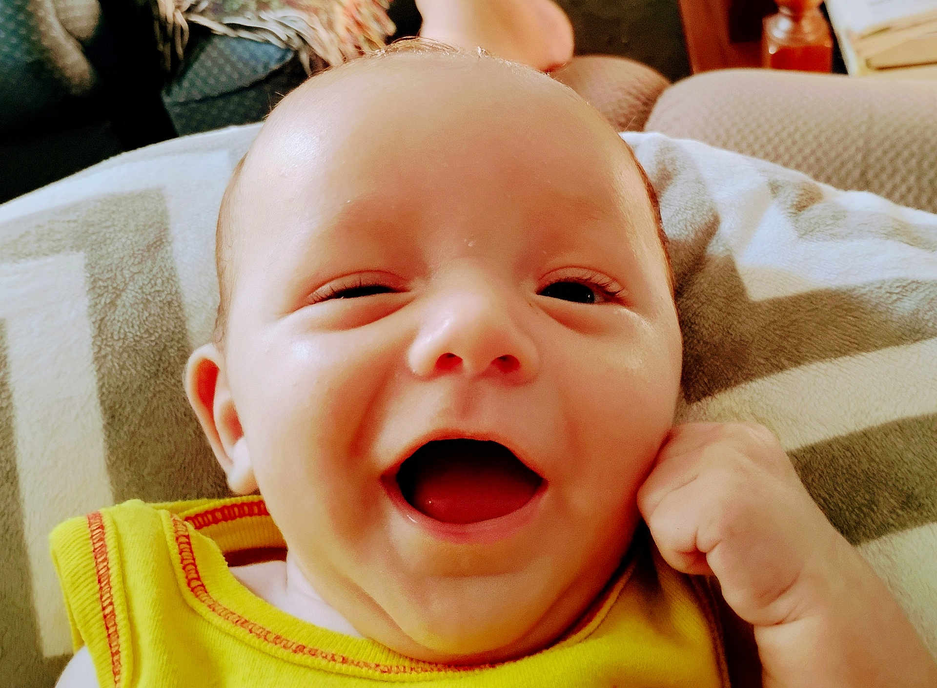 Elijah is registered to the contest to win money with this photo: baby, smiling, winking, yellow_clothing, face, infant, hand, blanket, indoor, happy, closeup, skin, furniture, couch, expression, child, portrait, cute, person, young