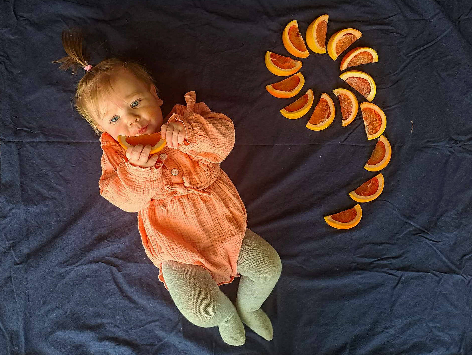 Everly is registered to the contest to win money with this photo: baby, baby_toddler_clothing, child, comfort, eye, finger, flower, gesture, hand, happy, head, linens, orange, peach, person, petal, product, sitting, sleeve, toddler