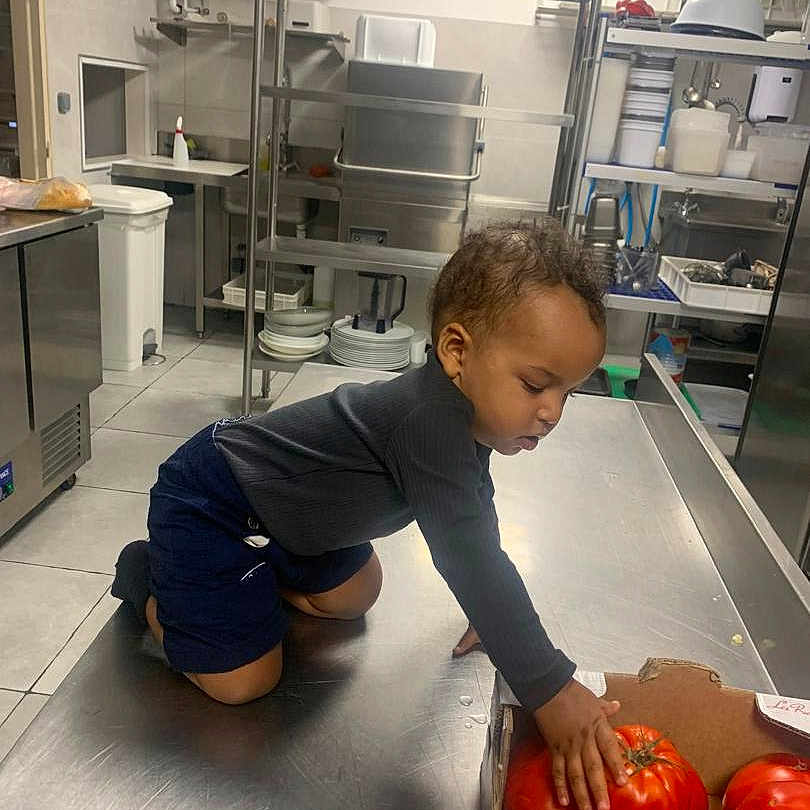 Alloux Nhesta a rejoint le concours — aidez-le/la à gagner de superbes lots ! child, clean, cooking_area, counter, crouching, curious, food, indoor, kitchen, long_sleeve, person, plates, produce, shelves, shorts, stainless_steel, toddler, tomatoes, utensils, young_child