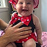 baby, smiling, polka_dot, hat, bow_tie, red_clothing, black_clothing, sitting, indoor, person, hand, cute, chubby, happy, infant, child, portrait, home, furniture, skin