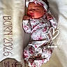 newborn, baby, sleeping, floral_clothing, headband, blanket, plush, portrait, infant, cute, peaceful, wooden_plaque, birth_details, soft_texture, indoors, resting, child, cozy, white_background, decorative_text