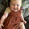 baby, barefoot, cheeks, child, couch, cute, dress, face, happy, indoors, infant, light_skin, patterned_fabric, person, plush, relaxed, short_hair, short_sleeves, sitting, smiling