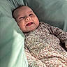 baby, infant, smile, face, onesie, floral_pattern, cushion, soft_fabric, sunlight, happy, child, portrait, closeup, indoor, cute, young_child, skin, head, expression, resting