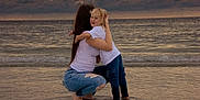 Karter joined the competition — help win amazing prizes! barefoot, beach, blonde_hair, casual_clothing, child, clouds, crouching, happy, hugging, jeans, long_hair, ocean, reflection, sand, shore, sky, sunset, water, white_shirt, woman