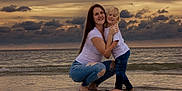 Karter is registered to the contest to win money with this photo: child, woman, beach, ocean, sunset, water, sky, clouds, casual_clothing, jeans, barefoot, hugging, smiling, family, nature, outdoor, portrait, emotion, love, togetherness