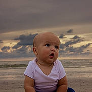 Kaden is registered to the contest to win money with this photo: baby, child, beach, ocean, sky, clouds, sand, sunset, sea, infant, portrait, curious, outdoor, nature, horizon, water, clothing, sitting, cute, young