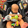 baby, car_seat, toy, plush_toy, infant, grocery_store, produce_section, shopping_cart, child, foot, hand, clothing, sitting, seatbelt, black_car_seat, indoor, shopping, cute, focused, childrens_toy