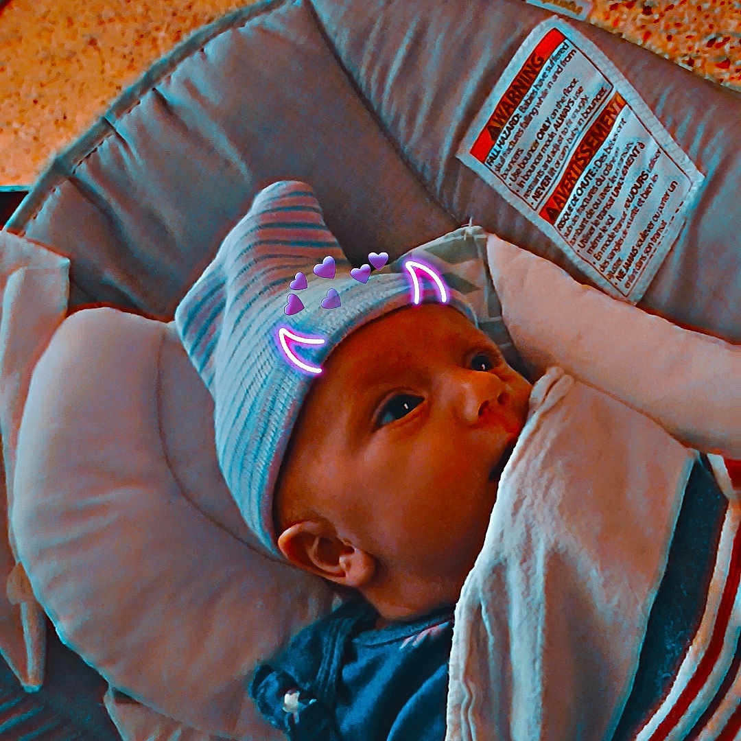 Tiberia is registered to the contest to win money with this photo: baby, blanket, child, closeup, clothing, cushion, cute, devil_horns, digital_filter, face, hand, hat, indoors, infant, newborn, portrait, purple_hearts, resting, seat, striped