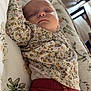 baby, sleeping, floral_clothing, maroon_pants, cushion, patterned_fabric, indoor, peaceful, child, portrait, soft_light, relaxing, infant, cozy, resting, home, cute, comfort, sleep, person