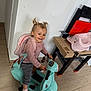 toddler, child, toy_scooter, pink_backpack, indoor, smiling, pigtails, playroom, toy_workbench, pink_potty_chair, floor, sneakers, happy, person, casual_clothing, wooden_floor, play, fun, young_child, cute