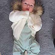 Isabel joined the competition — help win amazing prizes! baby, infant, blanket, clothing, sweater, fur, footed_pajamas, shoes, lying_down, face, head, person, portrait, soft_texture, gray_background, cute, young_child, comfortable, warm_clothing, indoors