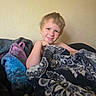 blanket, blue, casual, child, comfort, cozy, face, hair, happy, home, indoor, pattern, person, portrait, purple, relaxed, smiling, texture, wall, young