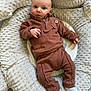 baby, infant, plush, cushion, brown_clothing, white_socks, face, portrait, indoor, soft_texture, cute, child, person, comfortable, lying_down, looking_at_camera, fleece, baby_clothes, cozy, expression