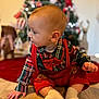Owen joined the competition — help win amazing prizes! baby, child, infant, plaid_shirt, red_overalls, socks, floor, christmas_tree, holiday, decorations, indoors, cute, portrait, seasonal, festive, young_child, sitting, wooden_floor, background_bokeh, cozy