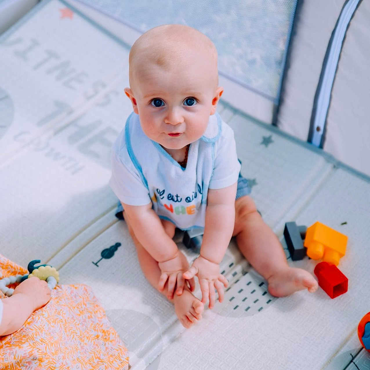 Lewenn a rejoint le concours — aidez-le/la à gagner de superbes lots ! baby, barefoot, blue_eyes, child, clothing, colorful, curious, cute, feet, floor, hands, indoor, infant, looking_up, person, plastic_toys, play_mat, sitting, soft_lighting, toys