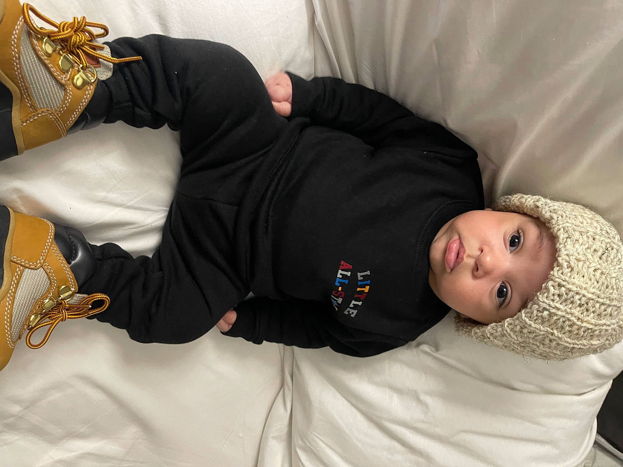 Baby Carlos is registered to the contest to win money with this photo: black_hair, comfort, cool, elbow, flash_photography, headgear, headwear, human_body, human_leg, joint, knee, leg, linens, person, room, sitting, sleeve, textile, thigh, trunk