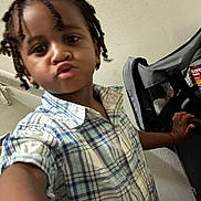 Jaleel is registered to the contest to win money with this photo: braids, casual, chair, child, cute, expression, face, hand, home, indoor, kid, person, person_holding, plaid_shirt, playful, portrait, smiling, toddler, wall, young