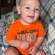 Jasper joined the competition — help win amazing prizes! baby, child, infant, smiling, happy, portrait, sitting, orange_shirt, plaid_couch, blanket, indoors, home, face, eyes, short_hair, barefoot, casual_clothing, playful, photography, couch