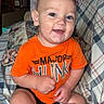 baby, child, infant, smiling, happy, portrait, sitting, orange_shirt, plaid_couch, blanket, indoors, home, face, eyes, short_hair, barefoot, casual_clothing, playful, photography, couch