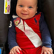 Gabriel-Moussa participe au concours pour gagner de l'argent avec cette photo : baby, infant, smiling, face, hands, car_seat, clothing, red_outfit, navy_sleeves, warning_label, airbag, cute, portrait, child, young, happy, seated, indoor, person, closeup