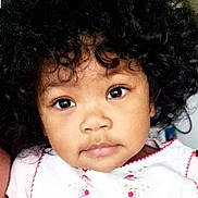 Monica joined the competition — help win amazing prizes! child, toddler, portrait, close_up, curly_hair, brown_skin, cute, eyes, face, expression, white_clothing, pink_embroidery, indoor, baby, young_child, person, innocence, adorable, headshot, looking