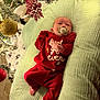 baby, infant, pacifier, red_clothing, christmas_tree, ornament, holiday, decorations, cushion, blanket, indoors, soft_lighting, festive, relaxing, cute, celebration, small_feet, newborn, holiday_season, cozy