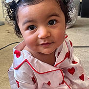 Anayla is registered to the contest to win money with this photo: toddler, child, face, curly_hair, flower_clip, pajamas, hearts_pattern, red_and_white, eyes, portrait, indoor, carpet, cute, smile, young_child, person, closeup, sitting, clothing, soft_light
