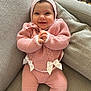 baby, smile, pink_clothing, knitted, bow, couch, grey_couch, happy, infant, cute, warm_clothing, indoors, child, hands_clasped, cozy, portrait, sitting, soft_texture, headwear, person