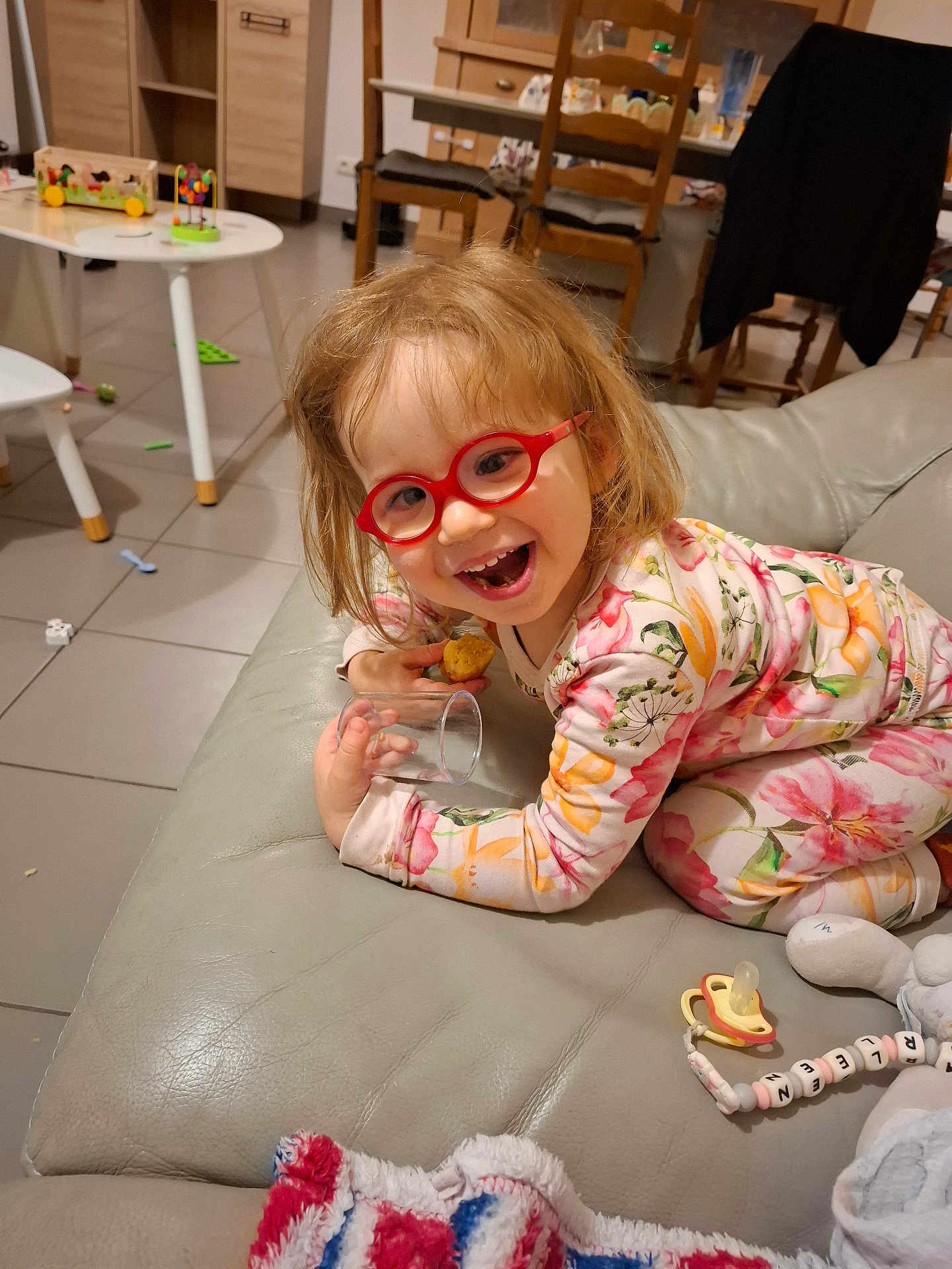 Charleen a rejoint le concours — aidez-le/la à gagner de superbes lots ! child, glasses, pajamas, couch, smiling, indoor, toy, table, chair, floor, snack, glass, hair, person, happy, living_room, pacifier, playful, cozy, furniture