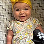baby, smiling, yellow_headband, floral_dress, zigzag_blanket, infant, cute, happy, portrait, child, closeup, face, eyes, cheeks, hand, pattern, soft_lighting, indoors, toy, playful
