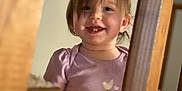 Pais is registered to the contest to win money with this photo: child, toddler, smile, teeth, bangs, purple_shirt, shirt, wooden_banister, staircase, indoor, portrait, close_up, happy, candid, home, railing, person, face, hair, young_child