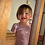 child, toddler, smile, teeth, bangs, purple_shirt, shirt, wooden_banister, staircase, indoor, portrait, close_up, happy, candid, home, railing, person, face, hair, young_child
