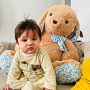 Shayan a rejoint le concours — aidez-le/la à gagner de superbes lots ! baby, child, plush_toy, stuffed_animal, bunny, couch, indoor, person, soft_toy, toddler, onesie, yellow_clothing, hand, face, fur, home, decor, seated, curious, expression