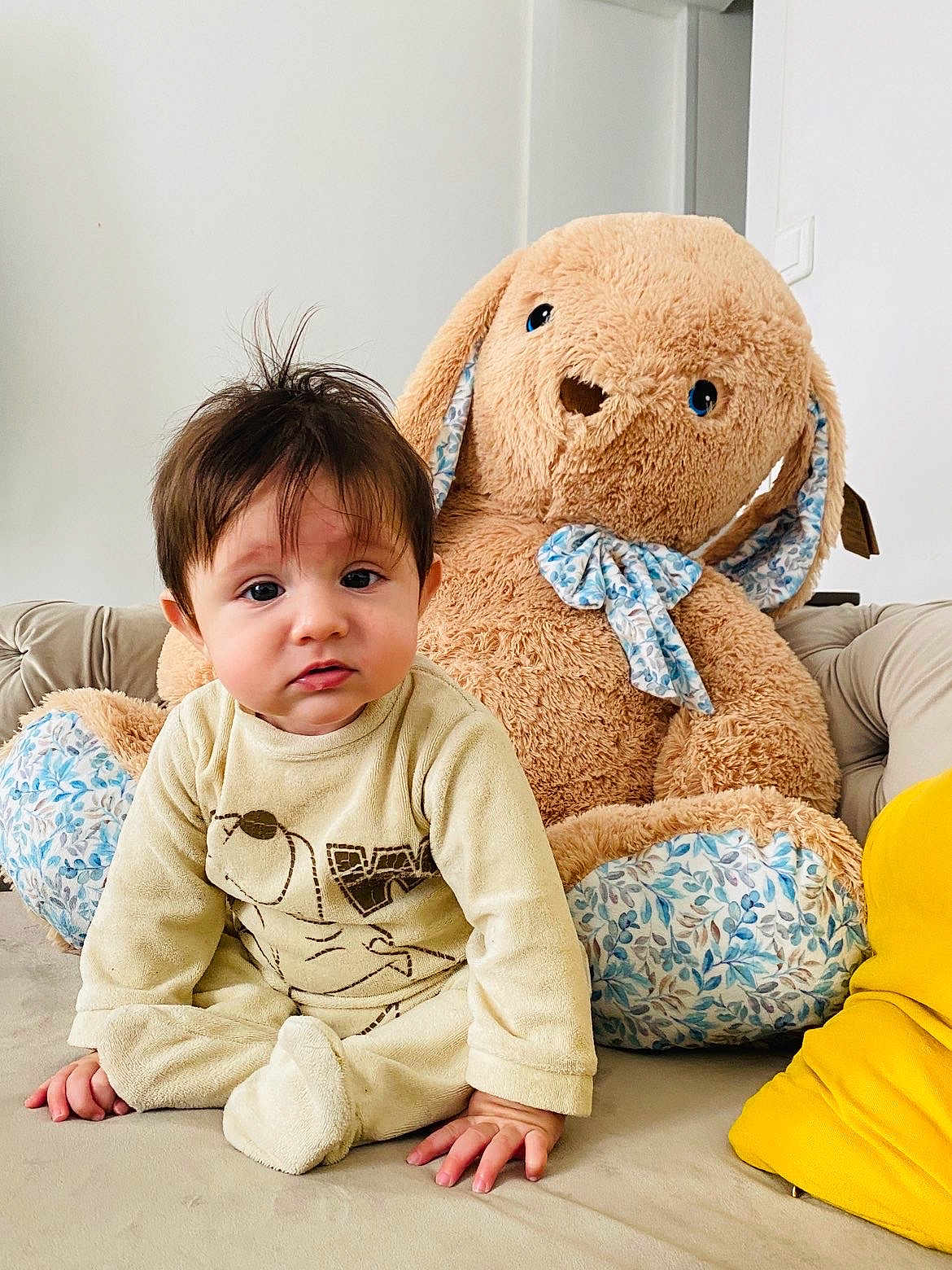 Shayan a rejoint le concours — aidez-le/la à gagner de superbes lots ! baby, child, plush_toy, stuffed_animal, bunny, couch, indoor, person, soft_toy, toddler, onesie, yellow_clothing, hand, face, fur, home, decor, seated, curious, expression