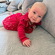 Kyla is registered to the contest to win money with this photo: baby, infant, red_dress, polka_dots, couch, gray_couch, indoors, living_room, child, face, smile, hand, blue_eyes, cute, cozy, soft_lighting, curious, portrait, toddler, home