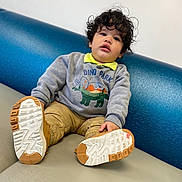 Dereck Gonzalez joined the competition — help win amazing prizes! child, toddler, curly_hair, sweatshirt, dinosaur, shoes, nike, couch, blue, gray, casual_clothing, indoor, portrait, smiling, young_child, sitting, comfortable, cute, playful, face