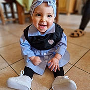 Inaya participe au concours pour gagner de l'argent avec cette photo : baby, child, smiling, sitting, headband, bow, blue_clothing, black_vest, white_shoes, indoor, tile_floor, happy, cute, person, infant, portrait, floor, furniture, slippers, blurred_background