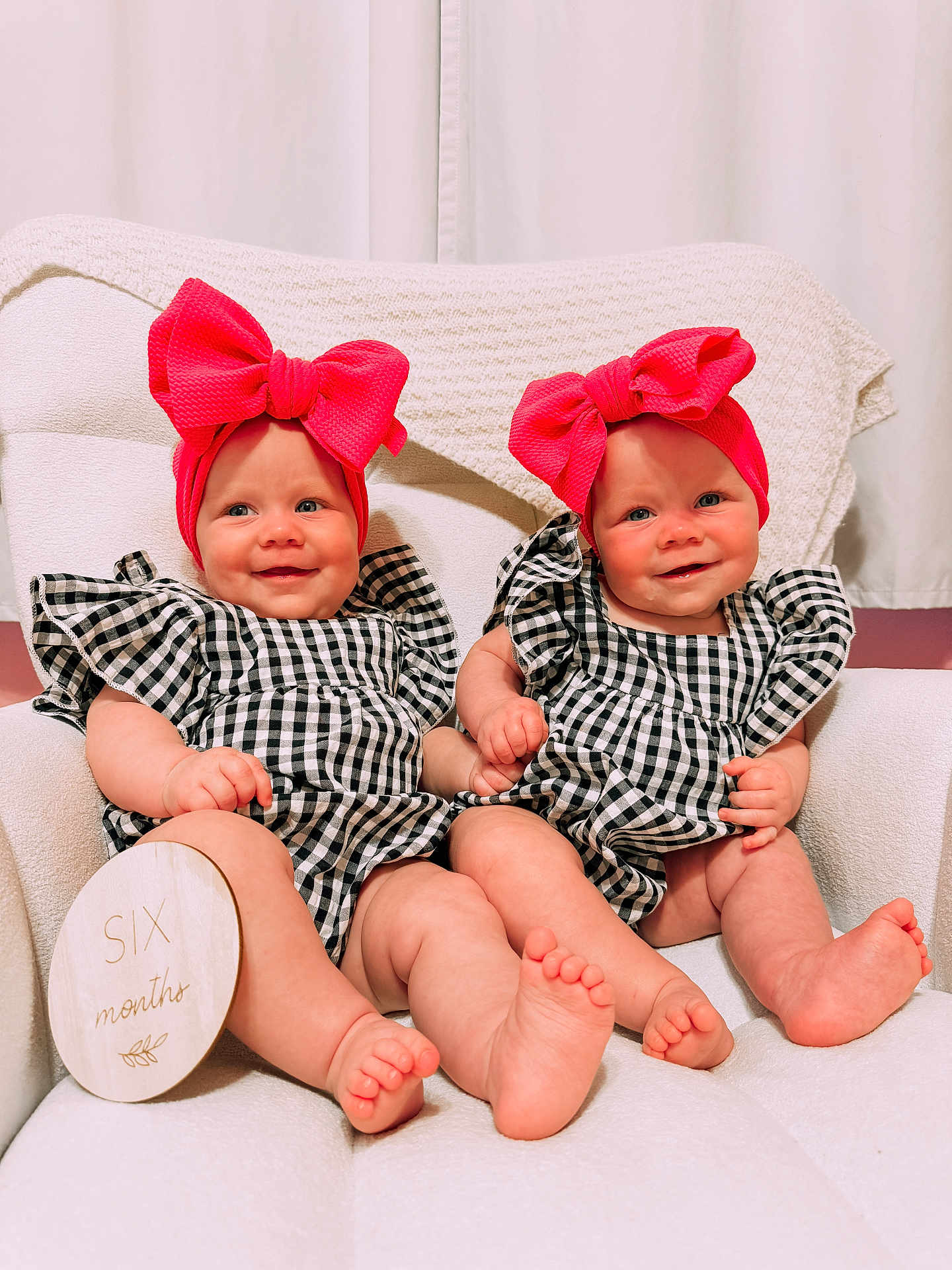 Lovelyn is registered to the contest to win money with this photo: baby, infant, twins, six_months, headband, bow, smile, holding_hands, checkered_clothing, white_chair, blanket, cute, portrait, indoors, child, feet, soft_lighting, happy, person, sitting