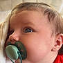 baby, close_up, pacifier, red_clothing, blanket, infant, face, cheek, hand, nose, ear, soft_texture, indoor, young_child, cute, skin, head, expression, comfort, portrait