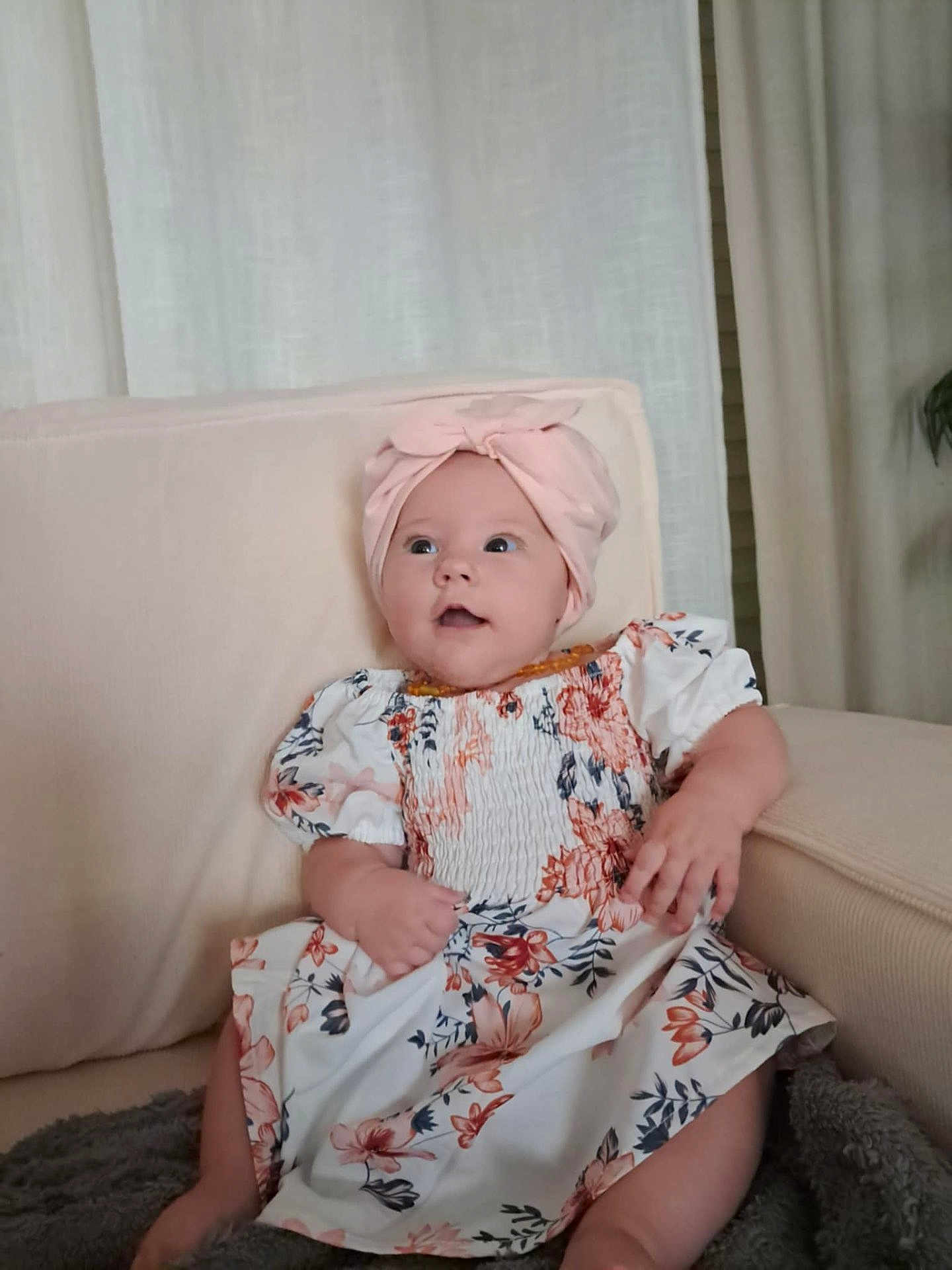 Louna a rejoint le concours — aidez-le/la à gagner de superbes lots ! baby, child, girl, headwrap, pink, floral_dress, couch, indoor, curtains, blanket, sitting, cute, portrait, smiling, happy, soft_light, home, comfort, hands, face