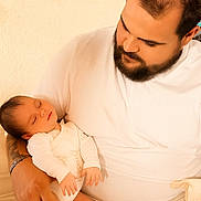 Lou a rejoint le concours — aidez-le/la à gagner de superbes lots ! baby, man, sleeping, beard, white_clothing, indoor, holding, person, family, parent, love, tender, infant, closeup, portrait, gentle, rest, warm_light, skin, care