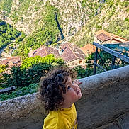 Nour-Elsa participe au concours pour gagner de l'argent avec cette photo : child, curly_hair, yellow_shirt, stone_wall, village, rooftops, hillside, greenery, outdoor, daylight, nature, scenic, portrait, looking_up, person, travel, landscape, young_child, cute, curiosity