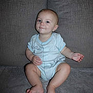 Titan is registered to the contest to win money with this photo: baby, child, infant, onesie, couch, gray, sitting, cute, face, skin, foot, hand, expression, young, indoors, smile, person, head, leg, blue