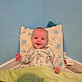 baby, smiling, blanket, pillow, indoor, child, happy, cute, cozy, floor, carpet, blue_wall, sleepwear, infant, face, sitting, home, comfort, toddler, colorful