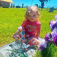 Natalie is registered to the contest to win money with this photo: child, toddler, portrait, outdoor, cemetery, church, gravestones, grass, flowers, butterflies, pink_shirt, floral_pants, sitting, curly_hair, blonde_hair, sunny, blue_sky, memorial, garden, face