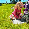 child, girl, toddler, smiling, happy, portrait, outdoor, cemetery, graveyard, gravestone, flowers, floral_arrangement, grass, sunny, daylight, pink_shirt, colorful_clothing, curly_hair, kneeling, memorial