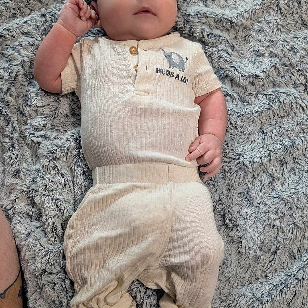 Achilles is registered to the contest to win money with this photo: baby, infant, clothing, blanket, soft_texture, lying_down, cute, portrait, child, cozy, elephant_print, fabric, feet, hands, looking_up, comfortable, casual_wear, indoor, relaxed, person