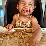 Stormie is registered to the contest to win money with this photo: toddler, child, smiling, happy, high_chair, chocolate, messy, face, hand, food, table, indoor, clothing, baby, cute, portrait, playful, dirt, fun, expression